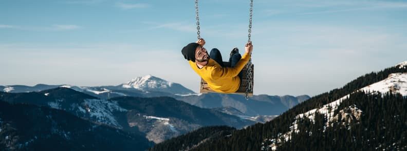 man enjoying the thrills of traveling alone while swinging over a mountain valley