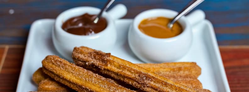 Close-up of sugar-dusted churros served with cups of hot chocolate and caramel in Madrid