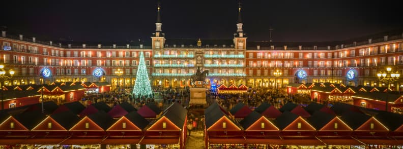 Plaza Mayor Christmas Market in Madrid lit up at night with a large tree and festive stalls