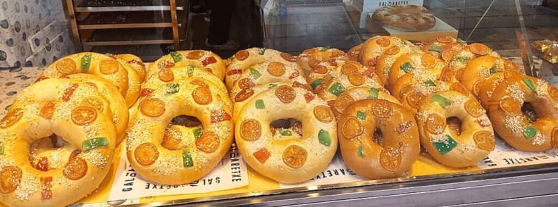 Rows of Roscón de Reyes cakes decorated with candied fruit in a Madrid bakery window