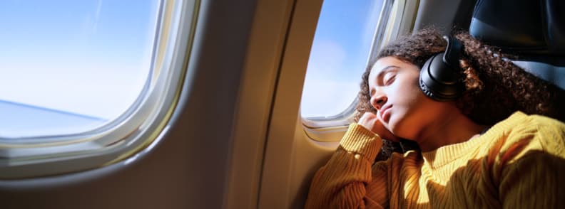 Back Sleeping Airplane Tips Ideal Recline Shoulder and Neck Support and Temperature Layering Passenger leaning back with headphones, resting in a window seat, illustrating back sleeping airplane comfort with ideal recline 100-120 degrees, shoulder and neck support plane techniques, and temperature layering plane clothing.