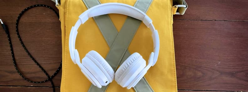 Best Accessories for Sleeping on a Plane Noise cancelling headphones Portable White Noise Machine Pink Noise App White noise cancelling headphones resting on a yellow travel bag for the best accessories for sleeping on a plane.