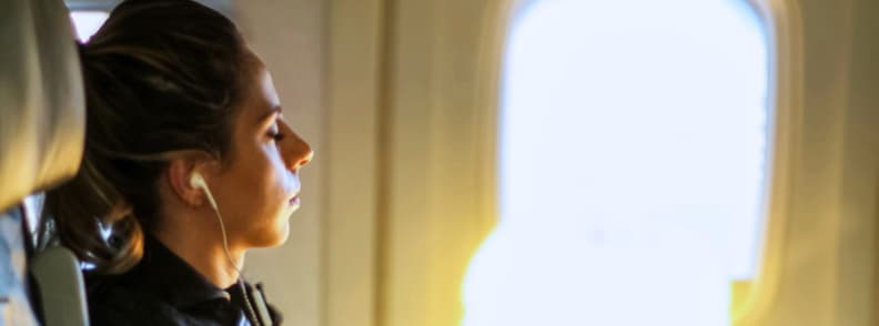 Best Seat Airplane for Sleeping Which Side of Plane Better for Sleep and Engine Noise Tips Woman resting in airplane window seat with earphones, showing the best seat airplane for sleeping, which side of plane better for sleep, and how to avoid a seat near engine noise.