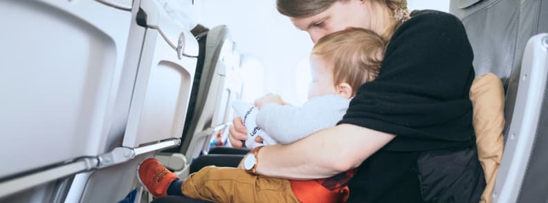 Kids Sleep on Plane Routine Tips for Parents Traveling with Children Mother holding a toddler in an airplane seat, showing how to follow a kids sleep on plane routine for smoother flights and better rest.