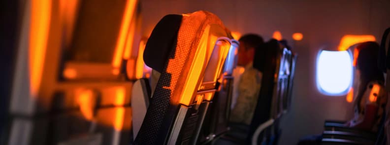 Strategy by Flight Type Daytime Flight Nap Airplane and Best Sleep Aid for Red Eye Flight Airplane cabin with dim lighting during sunset, showing passengers resting, illustrating strategy by flight type with daytime flight nap airplane tips and best sleep aid for red eye flight preparation.