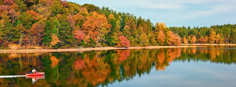 Person kayaking on a calm lake surrounded by colorful fall foliage reflecting in the water