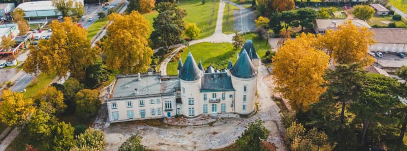 Aerial view of a French chateau surrounded by golden autumn trees showing affordable travel in off season Europe