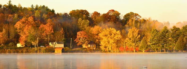 Golden trees reflecting on a calm lake at sunrise in Vernon Vermont during peak autumn foliage
