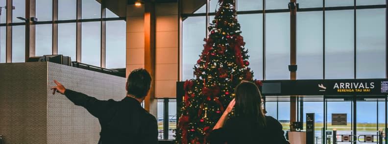 Travelers pointing toward a large decorated Christmas tree inside an airport arrivals hall