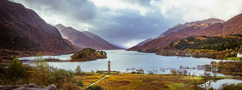 Glenfinnan Monument by Loch Shiel surrounded by autumn colors in the Scottish Highlands under dramatic skies