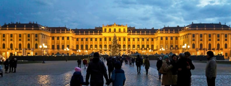 schonbrunn palace christmas market vienna winter evening Schönbrunn Palace Christmas Market lit up at dusk with a large Christmas tree and people walking through the illuminated courtyard