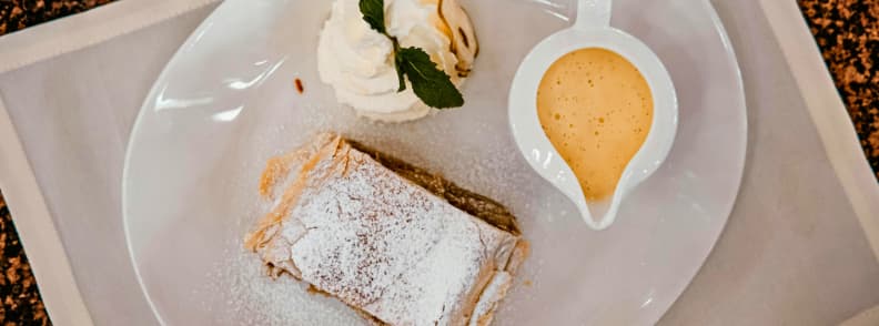 vienna apfelstrudel with vanilla sauce traditional dessert Classic Viennese Apfelstrudel dusted with powdered sugar served with whipped cream and vanilla sauce on a white plate