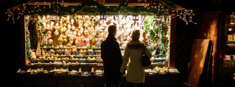 vienna christmas market couple ornaments night lights Couple standing in front of a brightly lit Christmas market stall in Vienna selling handcrafted ornaments at night
