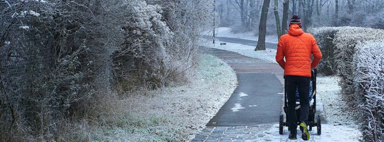 vienna winter walk parent stroller snowy park path Person in an orange jacket pushing a stroller along a snow-dusted path in a quiet Vienna park