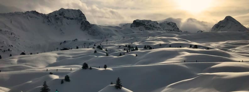 Belle Plagne Best Time to Ski France Soft rolling snowfields in Belle Plagne at sunset with scattered pines and high alpine peaks.