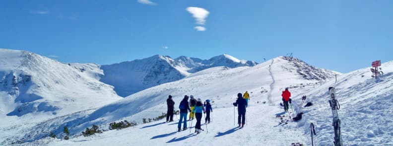 Borovets Bulgaria Winter Ski Slopes and Mountain Views Guide Skiers standing on a snowy ridge in Borovets with clear blue skies and the Rila Mountains in the background.