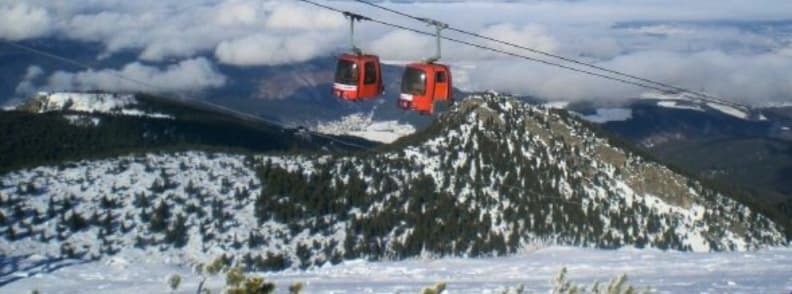 Bulgaria vs Alps Ski Costs Price Comparison Guide Red gondolas moving across a snowy mountain ridge in Bulgaria with clouds over the distant valleys.