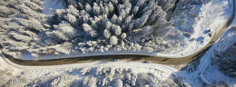 Driving to Bulgaria Ski Resorts Winter Roads and Transfer Guide Aerial view of a winter road winding through snow covered forest near Bulgaria’s ski resorts.