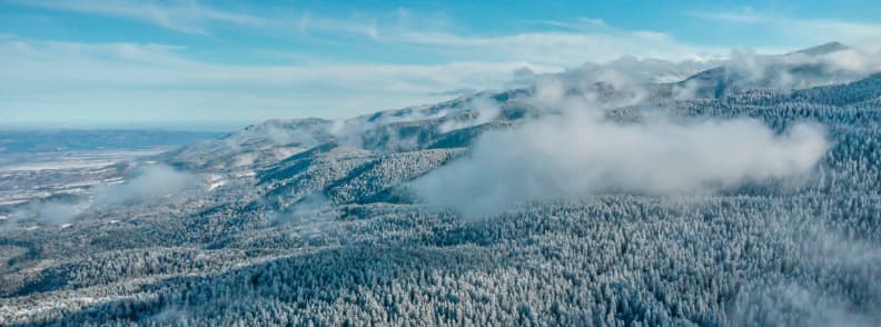 Off Slope Activities Bulgaria Ski Resorts Winter Guide Aerial view of snow covered forest and rolling mountains in Bulgaria with low winter clouds drifting across the ridges.
