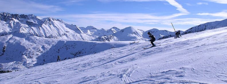 Skiing in Bulgaria. Skiers descending a wide snowy slope in Bulgaria ski resort with clear views of the Pirin mountain range on a sunny winter day.