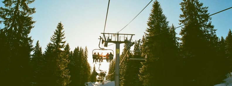 Skiing in France Avoriaz Forest Ski Lift Views Chairlift rising through snow covered forest in Avoriaz with skiers silhouetted against the afternoon sun.