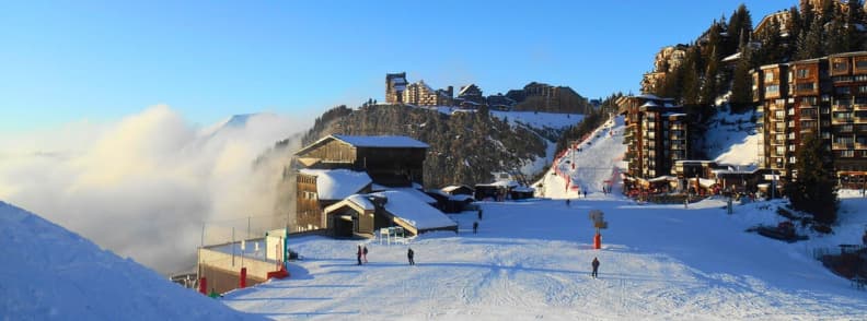 Skiing in France Avoriaz Snowy Village Slopes Skiers on sunny slopes in Avoriaz with wooden cliffside buildings and low clouds rolling through the valley.