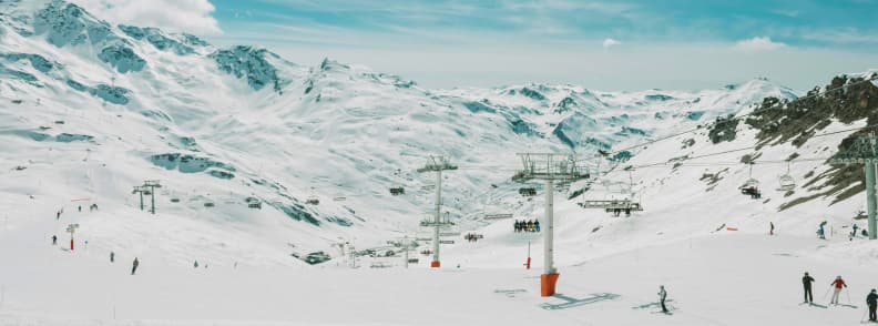 Skiing in France Best French Alps Ski Resorts Skiers on wide snowy slopes in the French Alps with chairlifts and mountain peaks under clear winter skies.