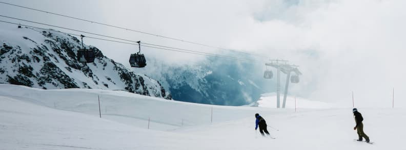 Skiing in France La Plagne High Altitude Snow Conditions Skiers on a misty high altitude slope in La Plagne with gondolas moving through clouds above the glacier ridge.