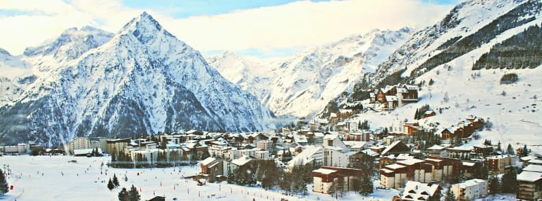 Skiing in France Les Deux Alpes Glacier Resort Les Deux Alpes village surrounded by snowy peaks with skiers on the lower slopes beneath the high Alpine glacier.