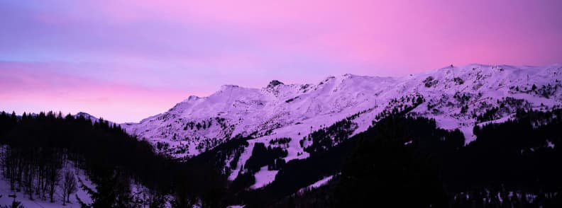 Skiing in France Meribel Sunset Alpine Views Pink and purple sunset over the snowy Méribel mountains with forested slopes in the French Alps.
