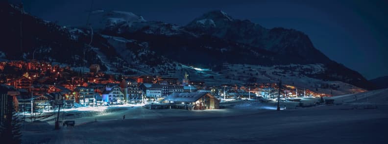 Skiing in France Montgenevre Nightlife Alpine Evenings Night view of Montgenèvre with illuminated village streets and surrounding mountains under a dark winter sky.