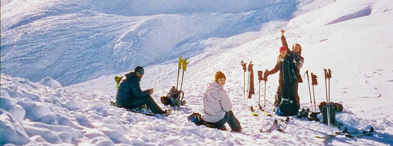 Skiing in France Off Piste Break French Alps Group of skiers resting on snowy terrain in the French Alps with poles and gear set in the snow.