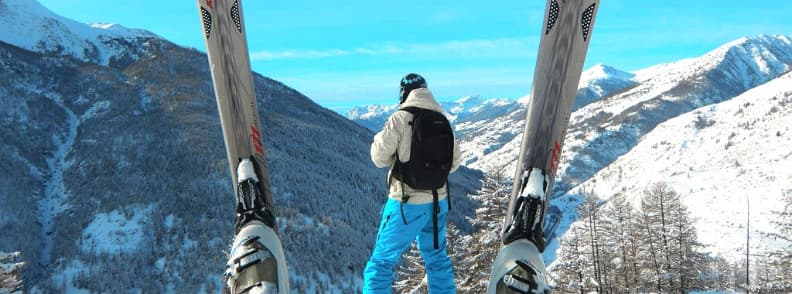 Skiing in France Snowboarding French Alps Viewpoint Snowboarder standing on a ridge in the French Alps with snow boards planted upright and snowy mountains in the background.