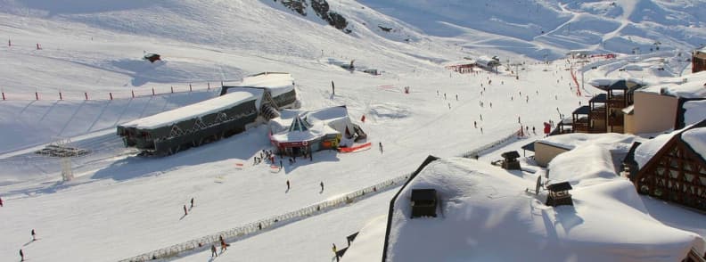 Skiing in France Val Thorens Highest Alpine Resort Val Thorens ski area with sunny high altitude slopes, skiers on wide pistes, and snow covered buildings in the village.