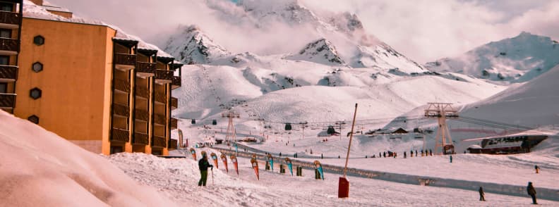 Skiing in France Val Thorens Ski in Ski Out Slopes Skiers on gentle slopes in Val Thorens with ski in ski out buildings and high snowy peaks rising behind the resort.
