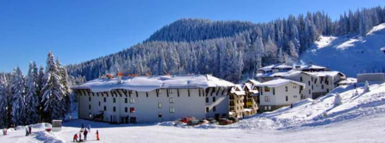 Sunshine Resort Pamporovo Bulgaria Ski In Ski Out Hotels and Sunny Winter Slopes Snow covered hotels at the base of a Pamporovo ski slope surrounded by pine forests on a clear winter day.