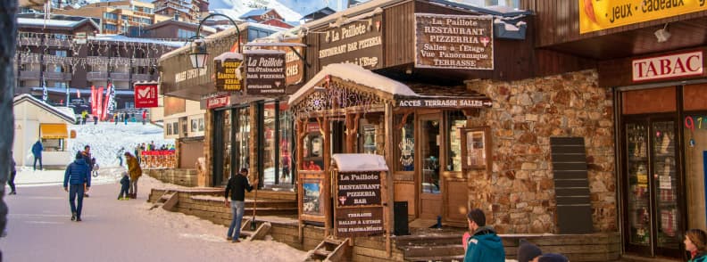 Val Thorens Dining Guide Restaurants in the French Alps Val Thorens village street with restaurants, pizzerias, and visitors walking between snowy alpine buildings.
