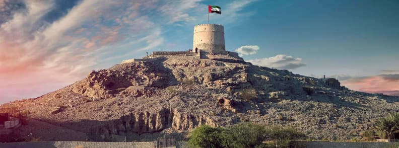 Hatta Fort historic landmark and heritage site UAE Hatta Fort tower with UAE flag on top of a rocky hill under blue sky