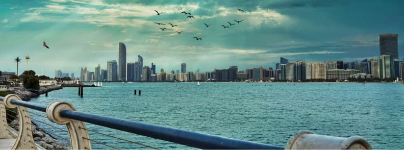 Abu Dhabi on a budget waterfront skyline view View of Abu Dhabi city skyline from the waterfront promenade with birds flying overhead