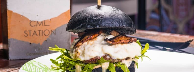 Cheap eats Abu Dhabi affordable restaurants guide Close up of a gourmet burger with black bun and melted cheese served at a budget friendly restaurant in Abu Dhabi