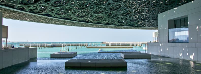 Louvre Abu Dhabi budget museum visit Interior view of the Louvre Abu Dhabi with its patterned dome and sea reflecting pools