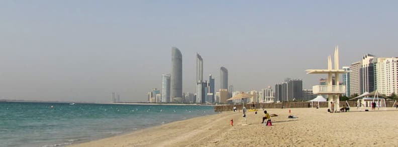 Families relaxing and walking along Abu Dhabi Corniche Beach with city skyline in the background