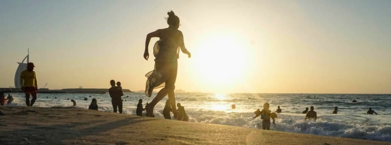 Families enjoying swimming and playing at a beach in Dubai during sunset with Burj Al Arab in the background