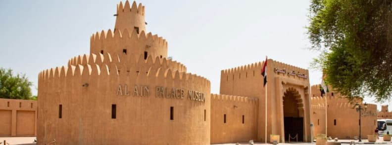 Exterior view of Al Ain Palace Museum with traditional fort walls and UAE flags under clear skies
