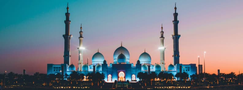 Sheikh Zayed Grand Mosque illuminated at sunset in Abu Dhabi with glowing domes and minarets