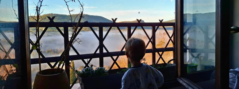 Life in Bagnols en Foret Provence Village with a Toddler My young son looking through our open window in Bagnols-en-Forêt, overlooking a mist-covered valley, wooded Provençal hills, and the wooden Parisian balcony railing.