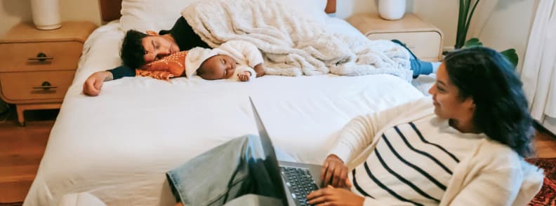 Family Travel Routine Rest and Recharge in Baby Friendly Accommodation Mother working on laptop while partner and baby nap in bed at cozy baby friendly accommodation while traveling with a baby