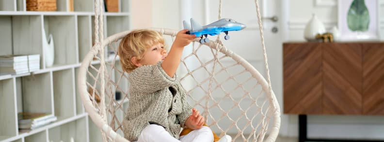 Flying with Toddlers guide for parents Young child sitting in a swing chair at home, playing with a toy airplane, capturing excitement and preparation for flying with toddlers