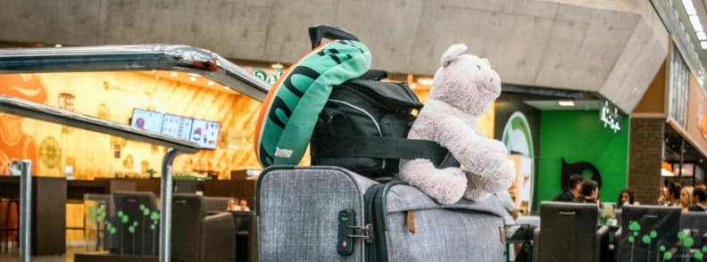 Luggage with toddler essentials at airport security checkpoint Toddler travel gear including backpack, stuffed animal, and neck pillow stacked on suitcase at airport, illustrating airport logistics and security screening for families