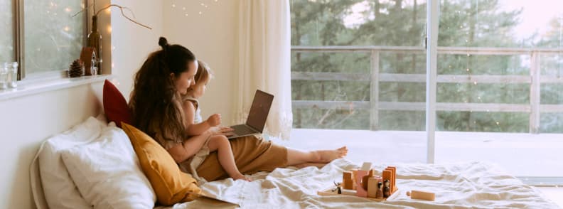 Parent booking toddler flight tickets online from home Mother and toddler sitting on a bed looking at flight options on a laptop, representing how to find deals, understand toddler flight costs, and compare airline policies